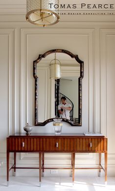 a large mirror hanging on the wall above a wooden table with a wine glass in front of it