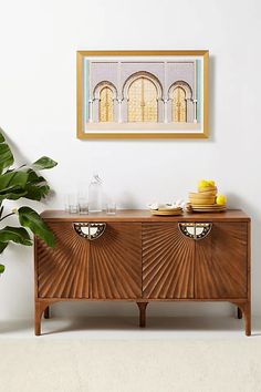 an art deco sideboard with plates and glasses on it in front of a potted plant