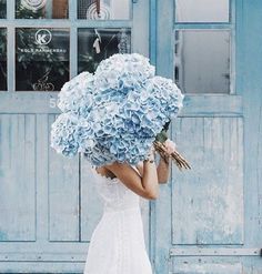 a woman in a white dress holding a large bouquet of blue hydrangea flowers