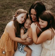 three girls hugging each other in the grass