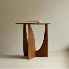 a wooden table with a book on top and a chair in the background, against a white wall