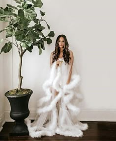 a woman standing next to a potted plant wearing a white dress with feathers on it