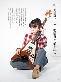 a young man sitting on the ground holding an electric guitar in front of his face