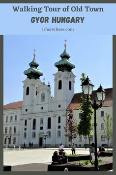 an old church with two towers and people sitting on a bench in front of it