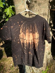 a t - shirt hanging on a tree in front of a tree with leaves and dirt all over it