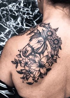 the back of a woman's shoulder with flowers and a horse tattoo on it