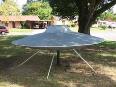 a large satellite dish sitting on top of a metal stand in the grass near a tree