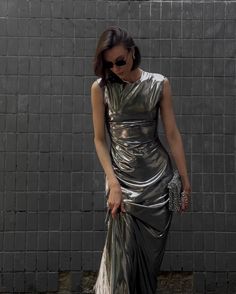 a woman in a silver dress is standing by a brick wall with her hand on her hip