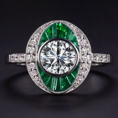 an emerald and diamond ring on a black surface with diamonds around it, in white gold