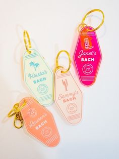 three different colored luggage tags are on a white surface and one has a gold keychain