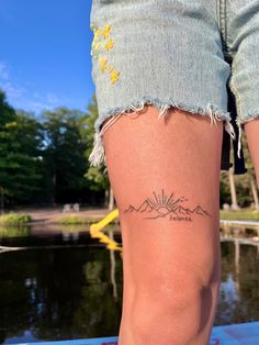 a woman's legs with a tattoo on the side of her leg and mountains in the background