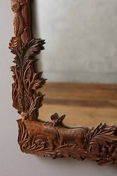 an ornate wooden mirror hanging on the wall next to a white wall and wood floor