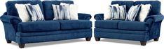 two blue couches with pillows on them sitting side by side in front of each other