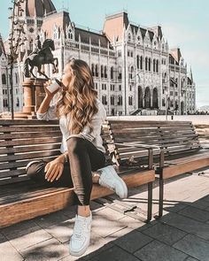 a woman sitting on top of a wooden bench next to a horse statue in front of a building