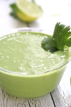 a green smoothie in a glass bowl with limes and parsley on the side