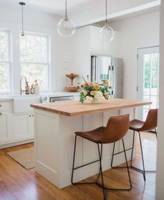 a kitchen island with two stools in front of it and flowers on the counter