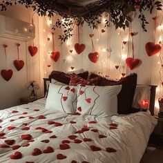 a bed topped with lots of pillows and red hearts hanging from the wall above it