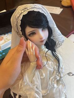 the doll is wearing a white dress and veil with her hands up to her face