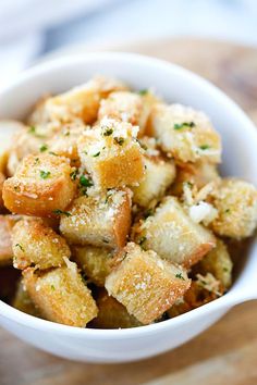 a small white bowl filled with bread and parmesan toppings on top of a wooden table