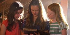 three girls looking at an open book together