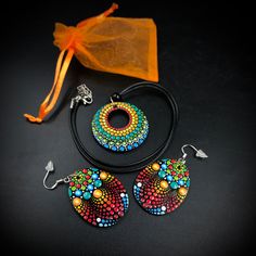 three pieces of beaded jewelry on a black surface next to an orange bag and drawstring