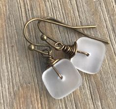 two white square glass beads hang from brass earwires on a wooden table top