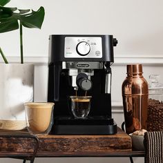 a coffee maker sitting on top of a wooden table next to a cup of coffee