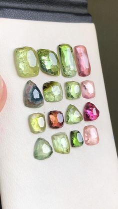 several different colored stones are arranged on a piece of white paper next to a hand