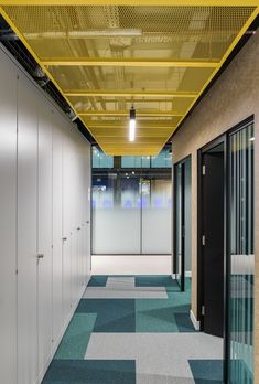 an empty hallway with blue and green carpeting, white walls and yellow ceiling lights