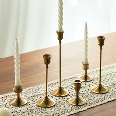 four candles are lined up on a doily with white and gold candlesticks