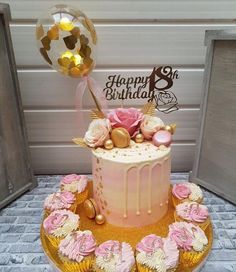 a pink and gold birthday cake with cupcakes on the bottom is surrounded by balloons