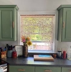 a kitchen with green cabinets and flowers in a vase on the window sill above the sink