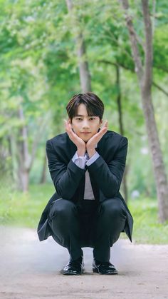 a young man in a suit kneeling on the ground with his hands to his face