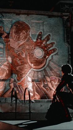 a person sitting on a bench in front of a wall with an image of a giant spider man