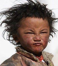 a young child with hair blowing in the wind and mud on his face is looking at the camera