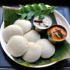 some food is on a white plate with green leaves and sauces in small bowls