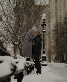 two people standing in the snow next to a street light