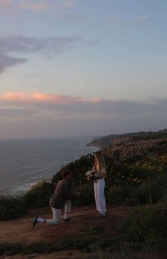 two people standing on top of a hill next to the ocean