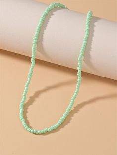 a green beaded necklace sitting on top of a white piece of paper next to a roll