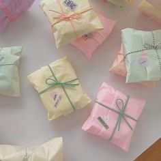 many wrapped presents are sitting on the table with ribbons and tags tied around them, all in pastel colors