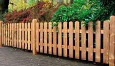 a wooden fence in the middle of a brick walkway next to some trees and bushes