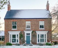 a large brick house with white windows and blue door in the snow covered yard area