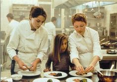 two women and a girl are in the kitchen preparing food on plates with utensils