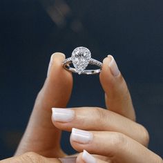 a woman's hand holding a diamond ring in front of her face with white nails