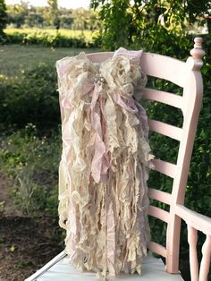 a white chair with a pink ruffled pillow on it's back sitting in front of a tree