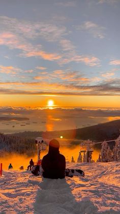 a person sitting on top of a snow covered slope with the sun setting in the background