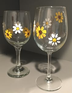 two wine glasses with yellow and white flowers painted on the glass are sitting next to each other