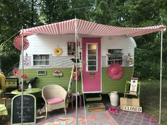 a small green and pink trailer parked in front of a tree filled field with furniture