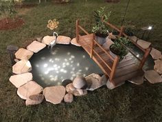 a small pond in the middle of a yard with rocks around it and lights on