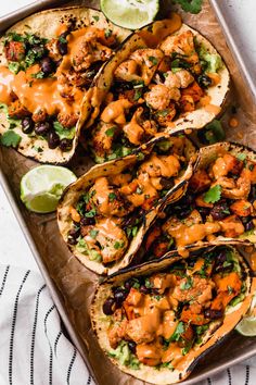 chicken tacos with guacamole and lime wedges on a baking sheet